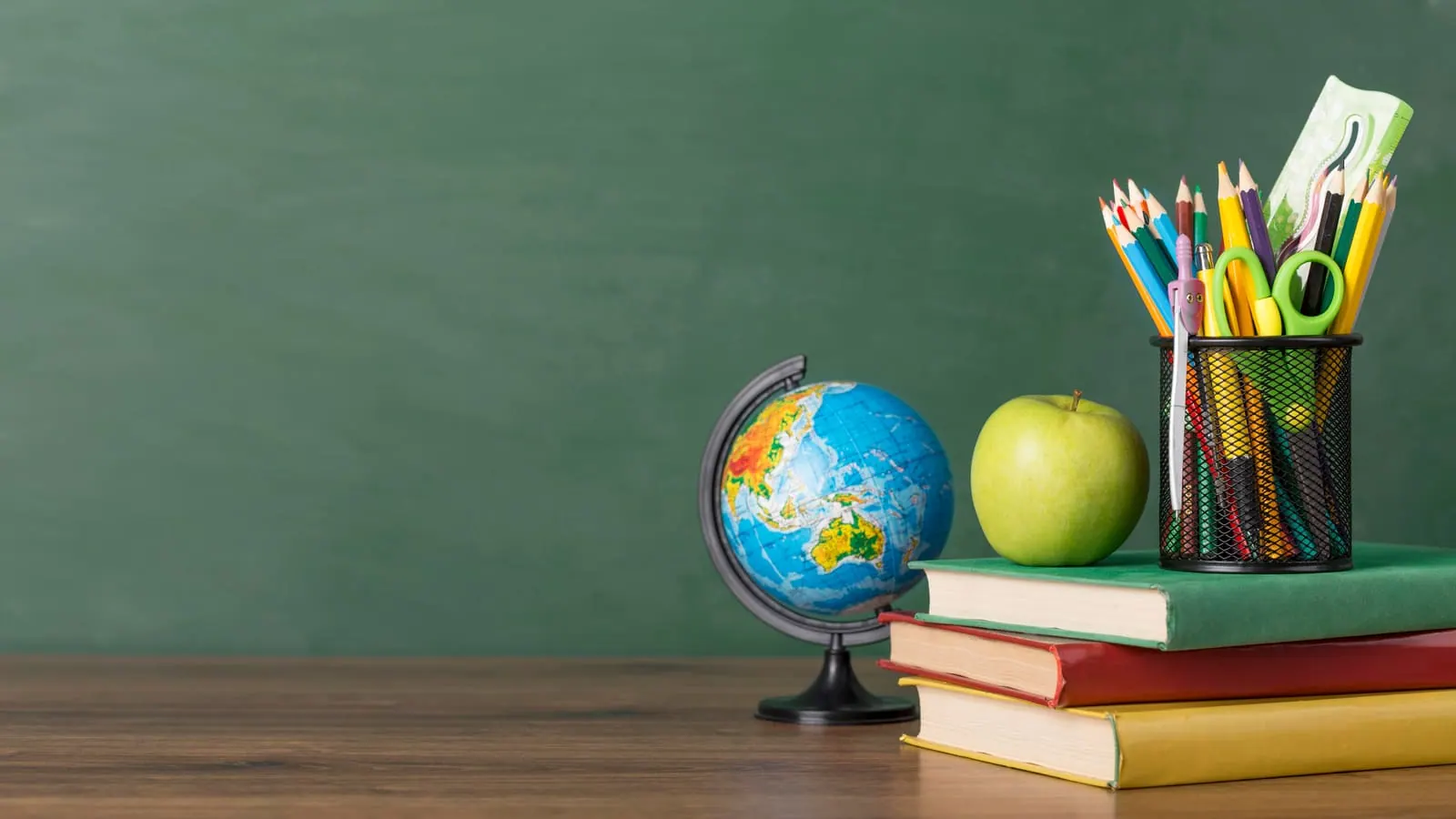 A globe, an apple, books and a cup of pencils on a desk