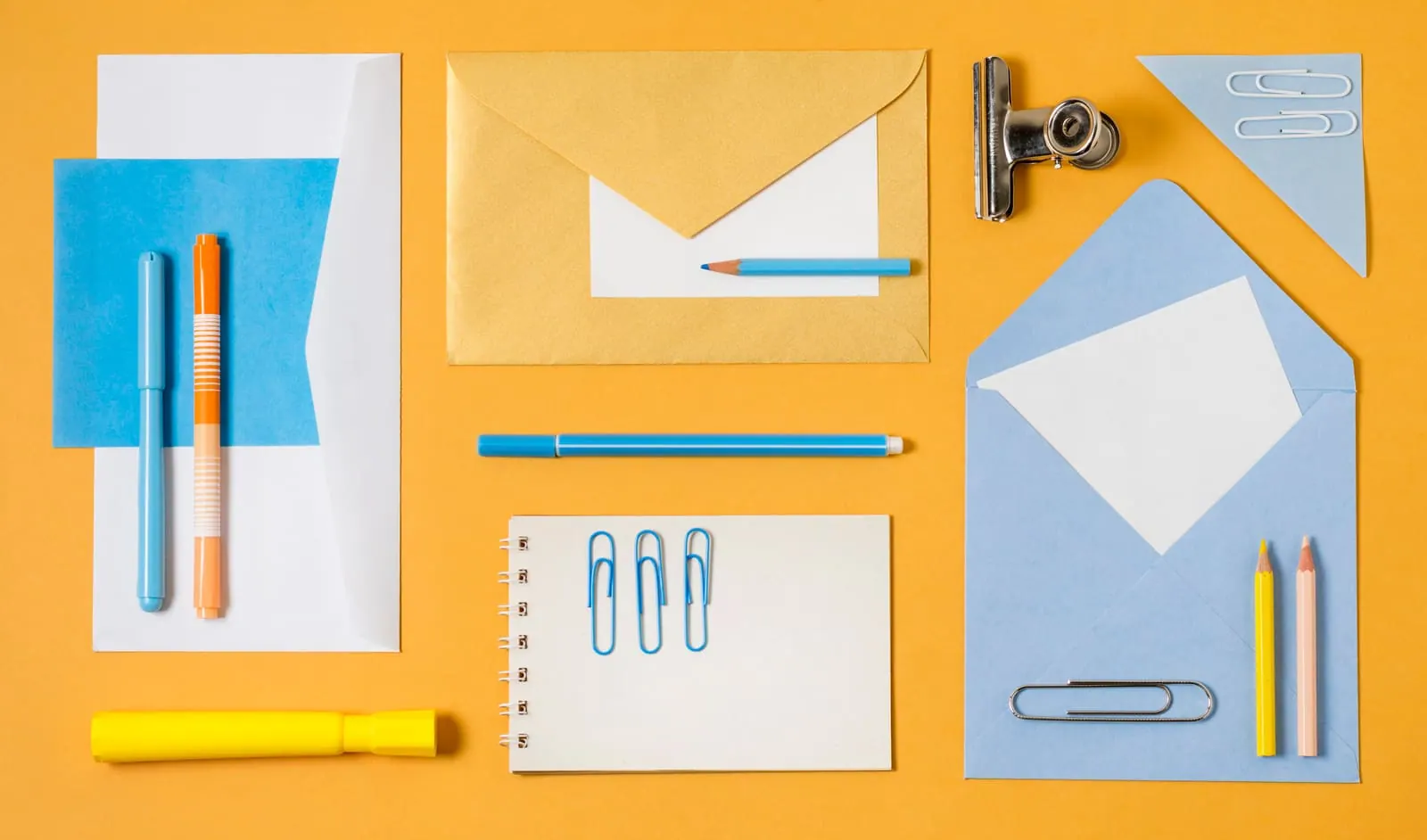 Envelopes, notepads, paper clips and pencils laid out flat on a yellow desktop