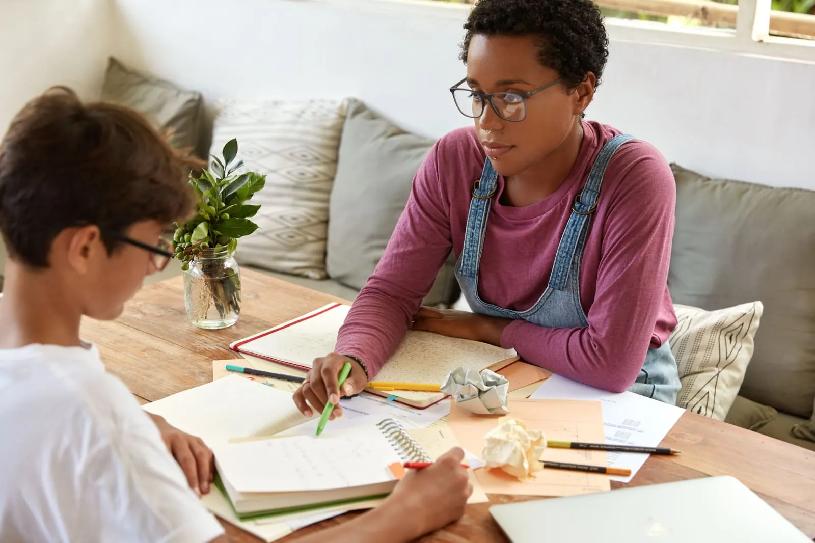 An adult sitting beside a student who is writing in a notebook at a table