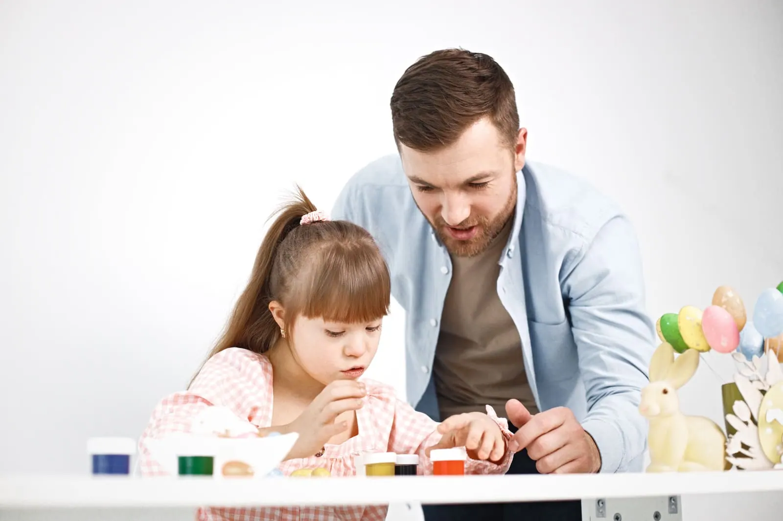 A teacher helping a young girl with a painting activity at a table