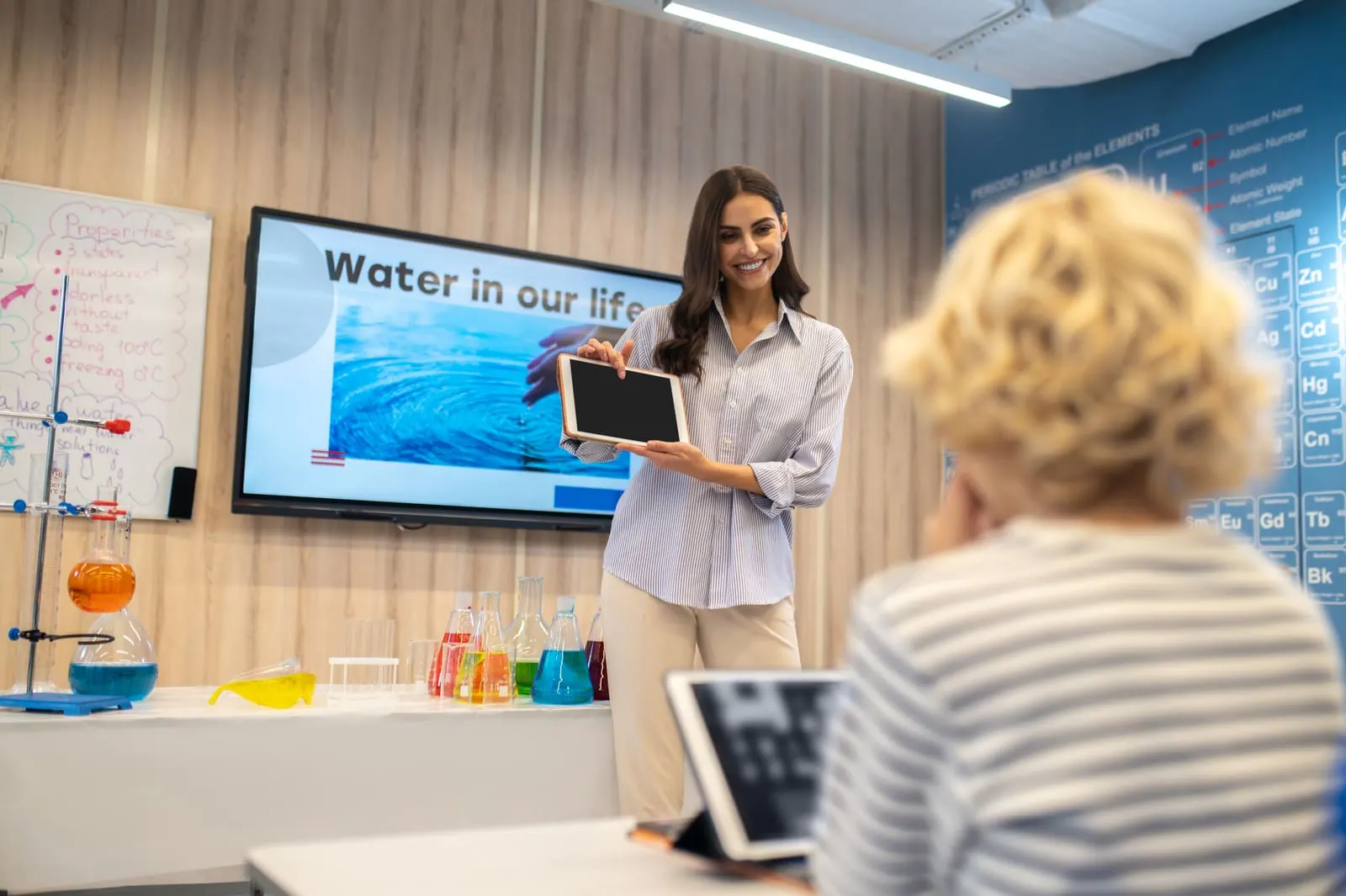 A teacher holding a tablet beside an interactive display in a classroom