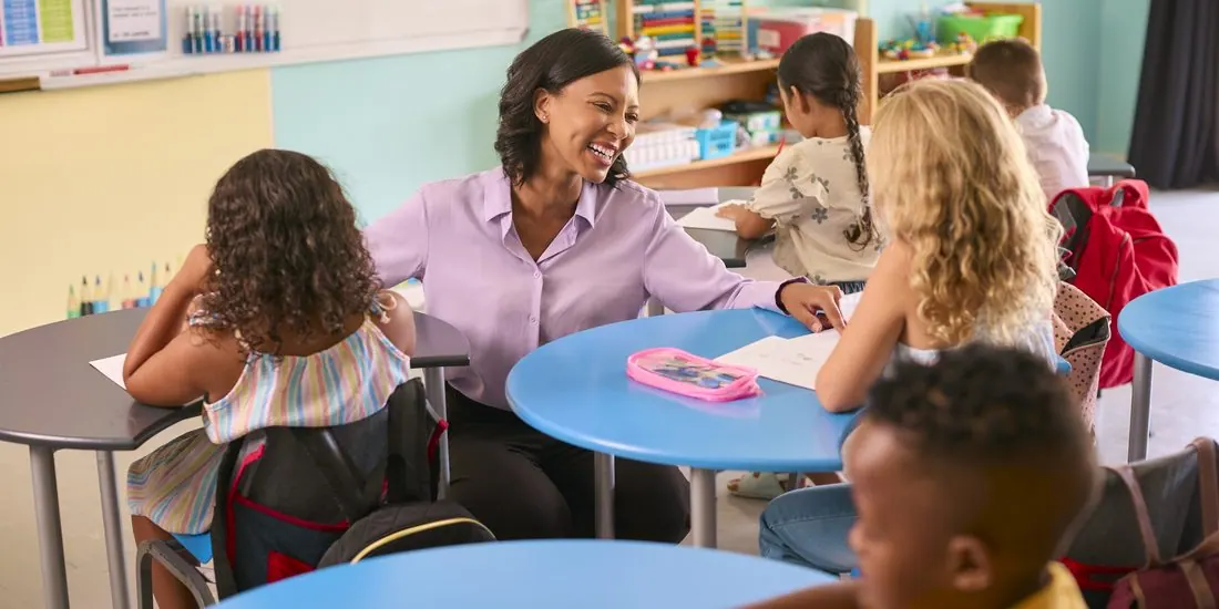 An elementary teacher helping students at a round classroom table