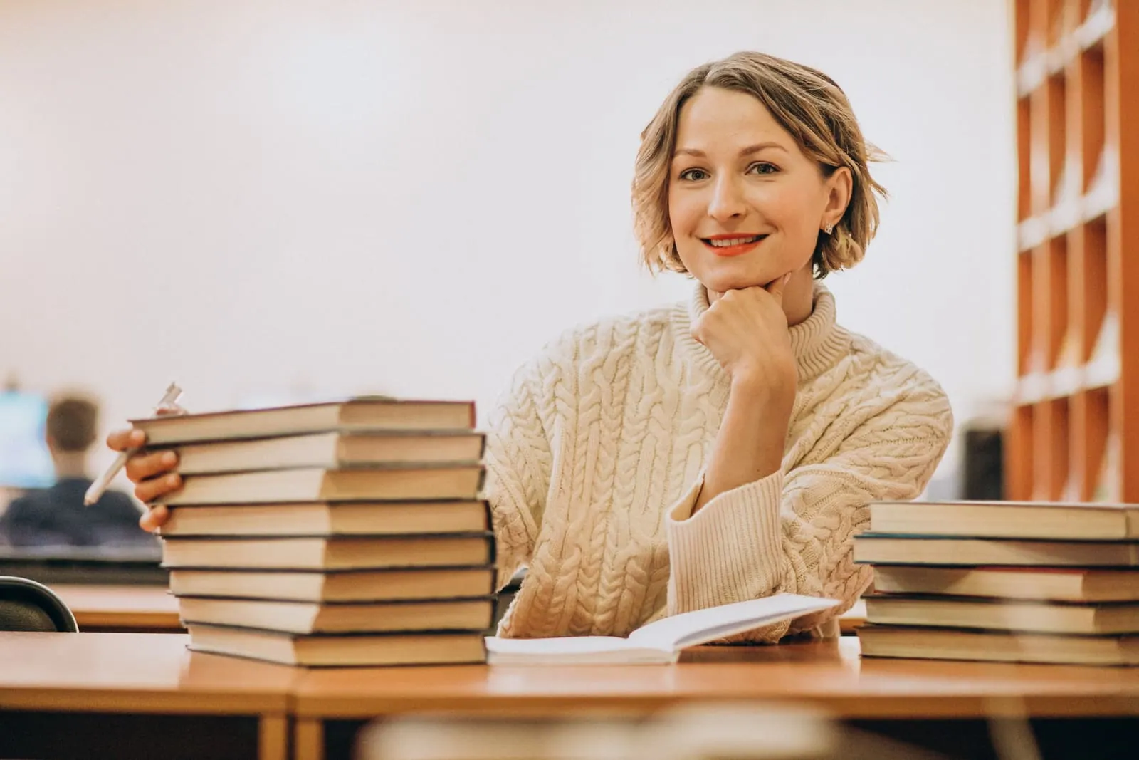 A smiling educator seated at a desk beside a stack of books