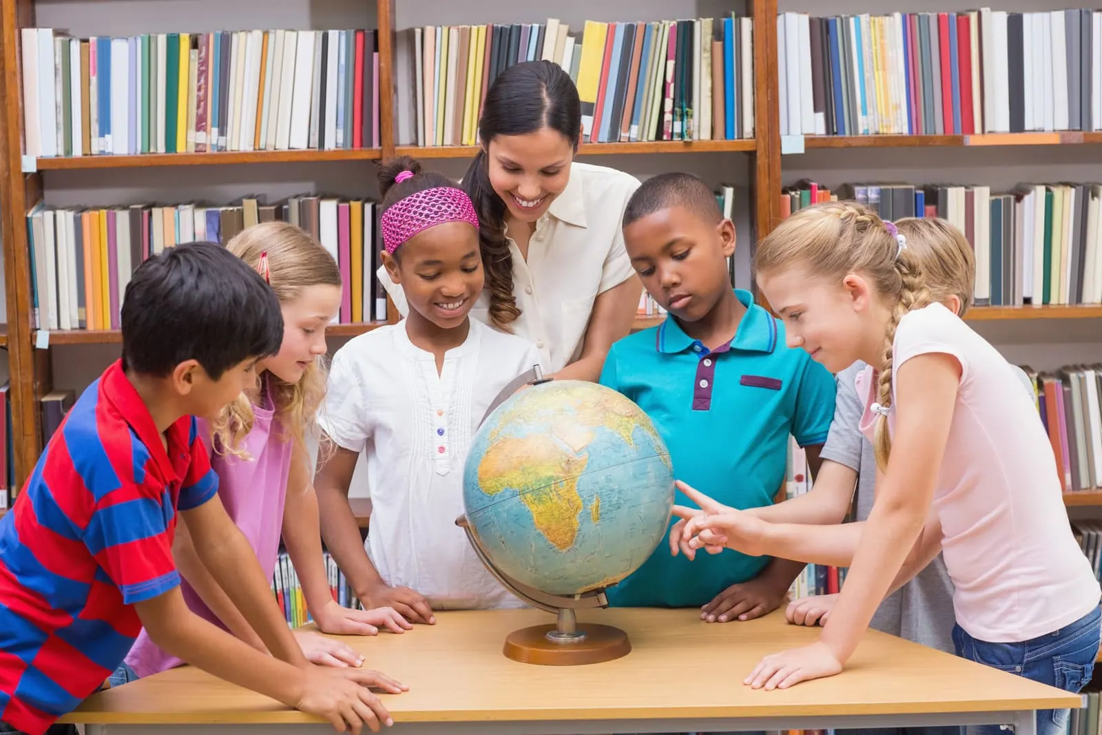 A teacher and students gathered around a globe in a library