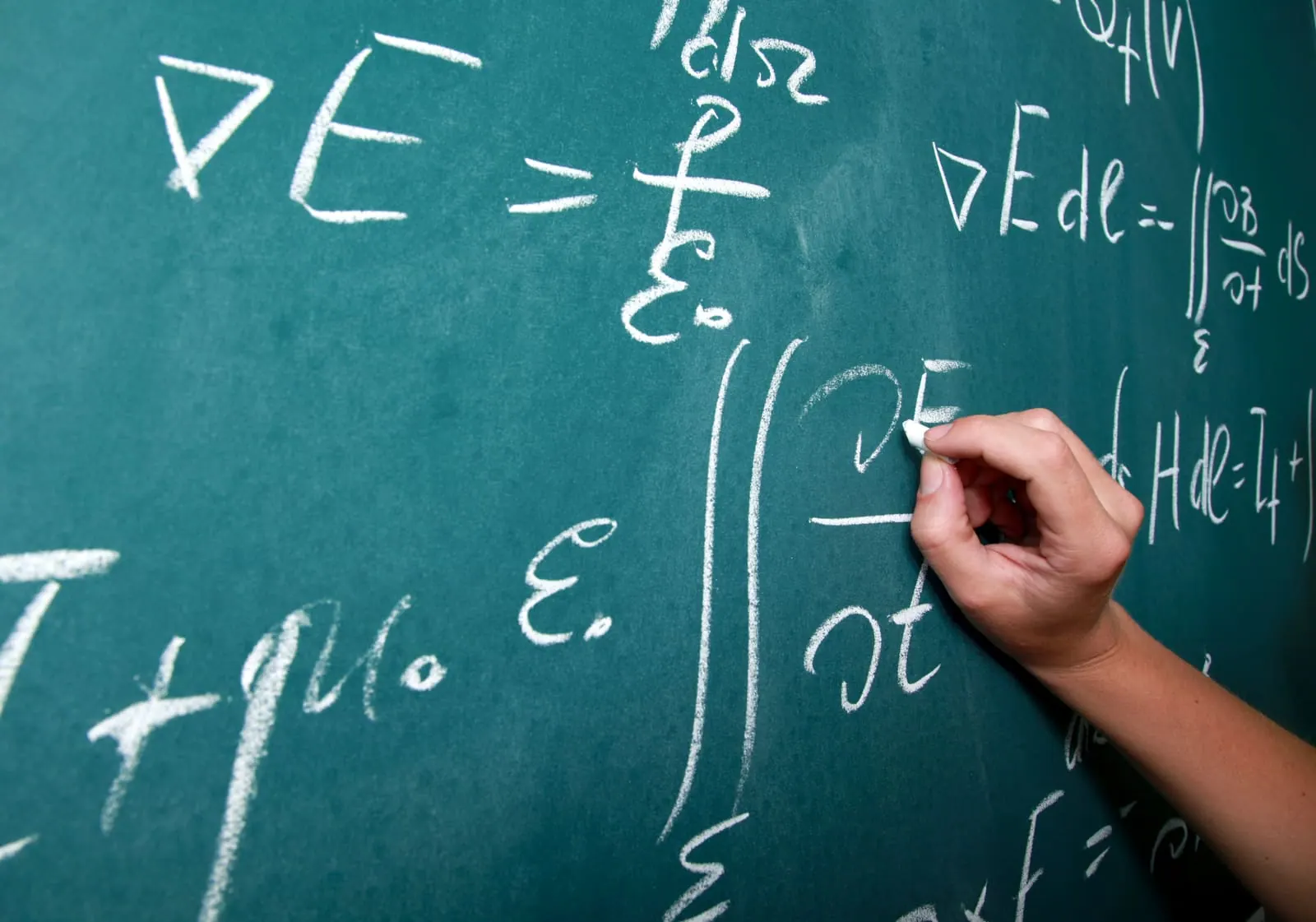 A hand writing equations on a green chalkboard