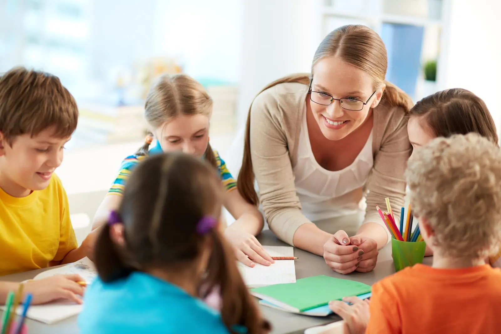 A teacher leaning over a table to work with a group of young students