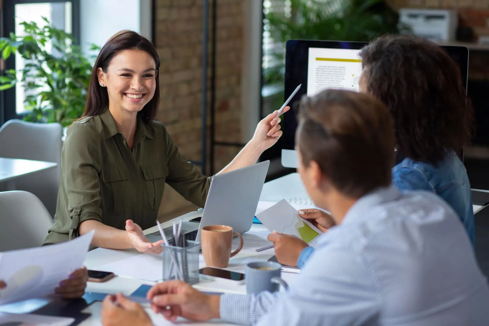 A woman pointing at a computer screen during a meeting of colleagues around a table
