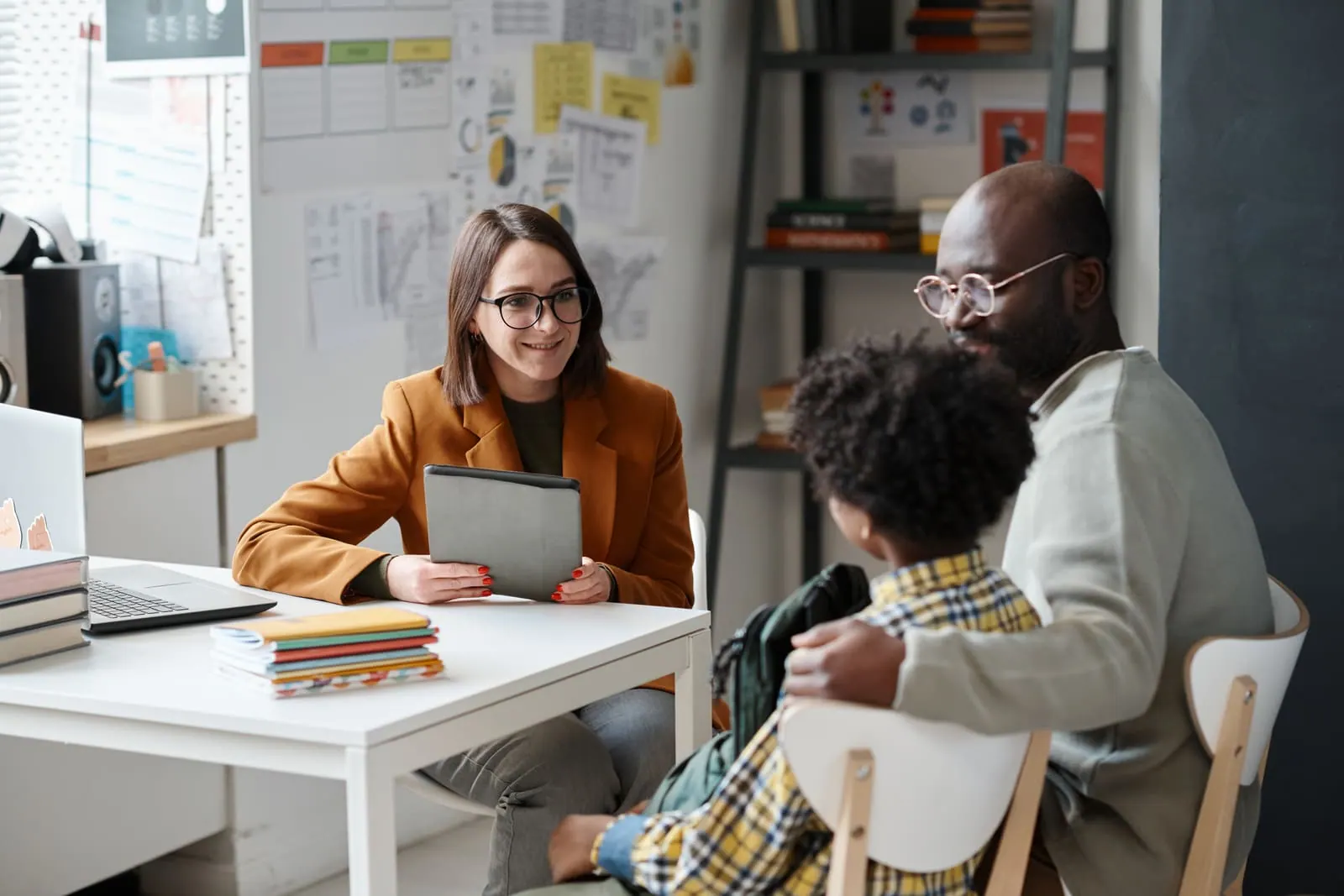A woman holding a tablet at a desk, talking with an adult and a child